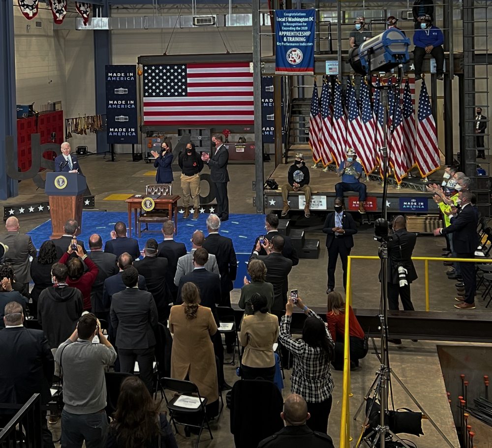 President Biden speaks to a small crowd of steelworkers with a large American flag in the background