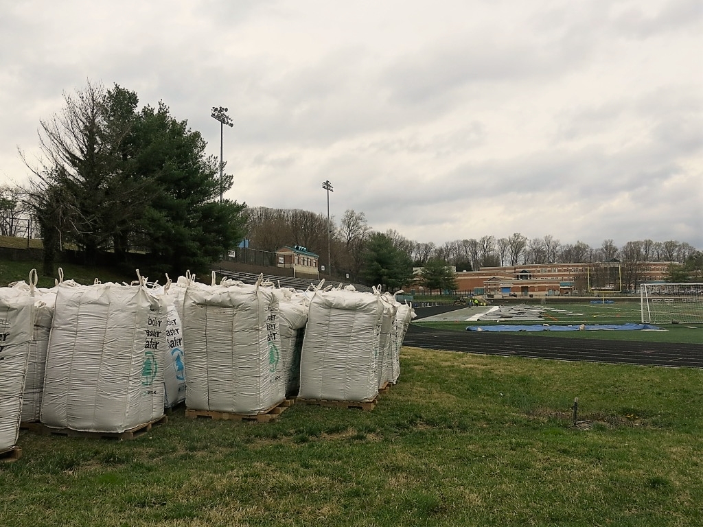 bags of field infill at the edge of a synthetic turf field